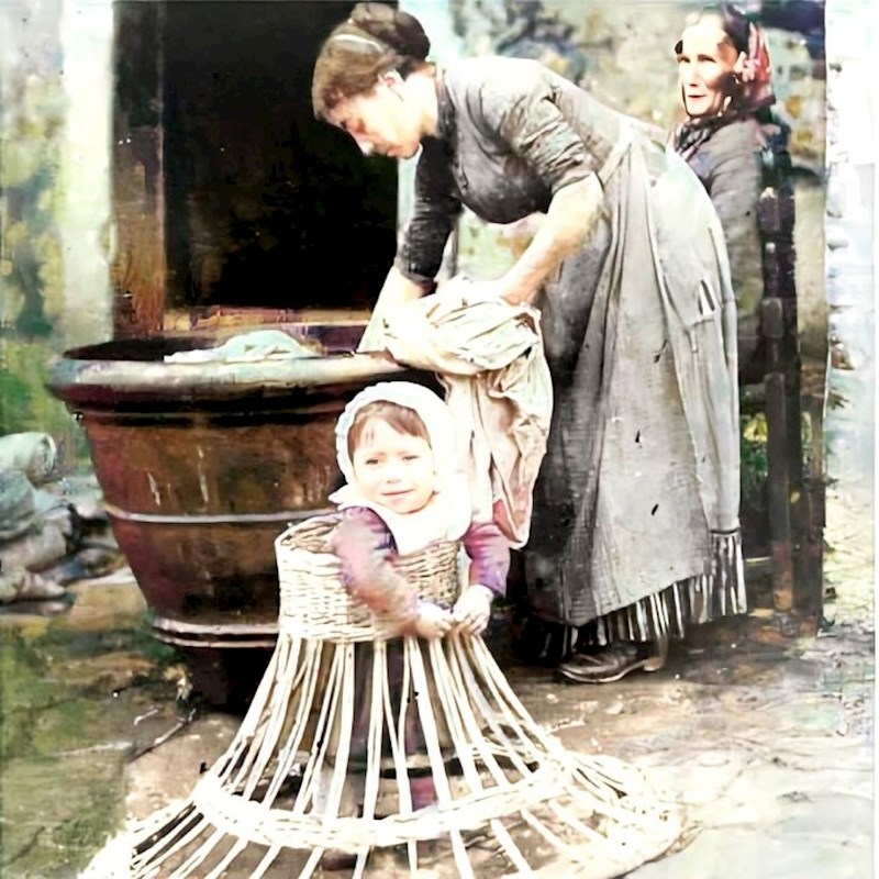 Beba uči hodati u okviru od pruća dok mama pere rublje. 1910-ih