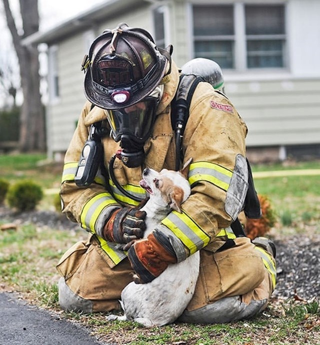 Vatrogasac tješi psa kojeg je spasio iz kuće koju je zahvatio požar.