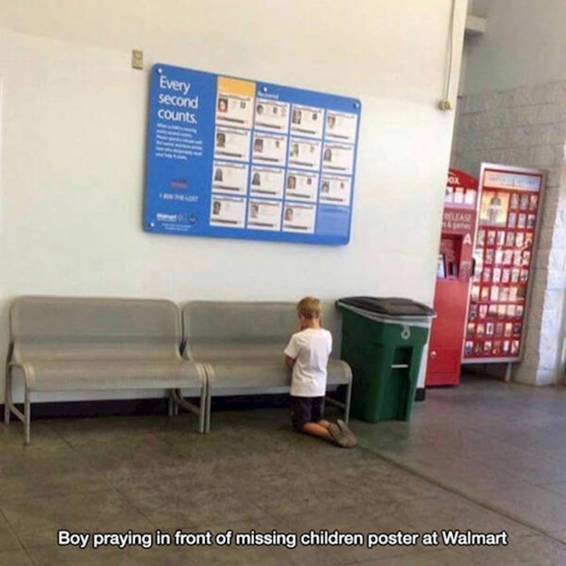 16. Klinac koji se moli ispred plakata na kojem su prikazana nestala djeca