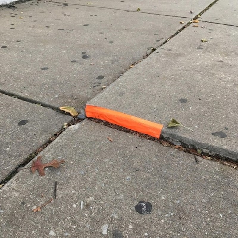 Netko je zalijepio narančastu traku na izdignuti dio pločnika kako ljudi ne bi upadali.