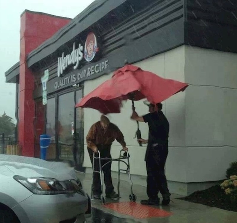 Ovaj radnik štiti starijeg gospodina od kiše.