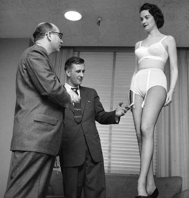 Kupac gleda novi grudnjak i gaćice za ženu na modelu u dućanu, 1955.