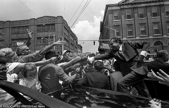 Predsjednik SAD-a Richerd Nixon stoji na braniku auta kako bi se mogao rukovati s ljudima.