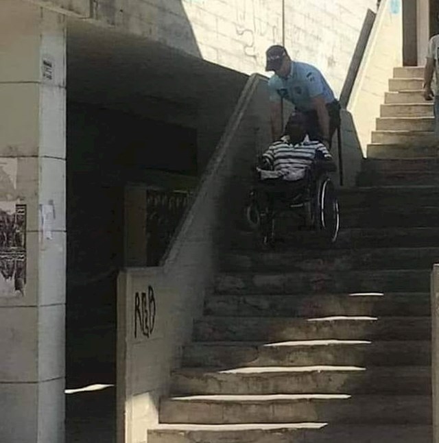 Policajac pomaže invalidu da se spusti niz stepenice.