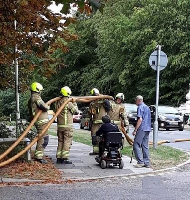 15. Vatrogasci drže crijevo kako bi žena u invalidskih kolicima nesmetano prošla.