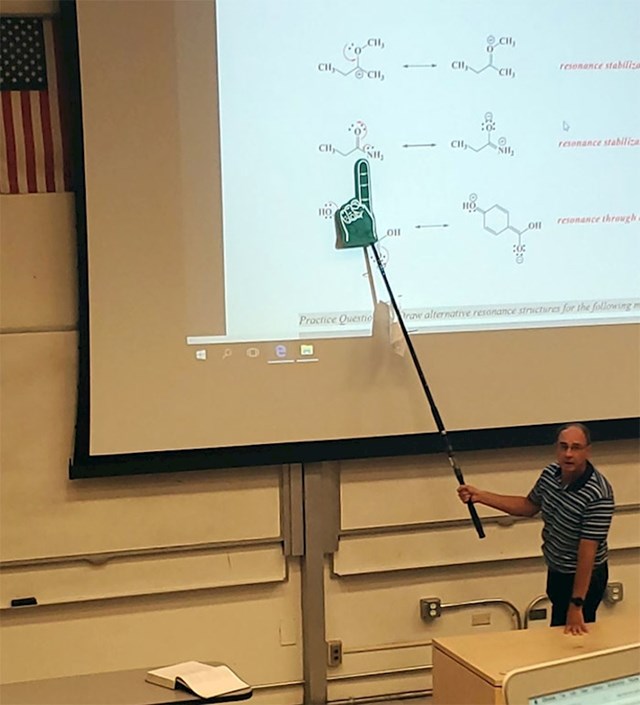 "moj profesor koristi ribolovni štap s pričvršćenim prstom od pjene za pokazivanje na ploču"
