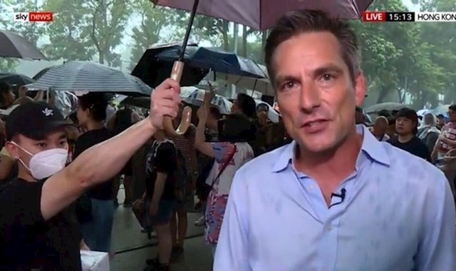 Sudionik protesta pridržava kišobran izvjestitelju